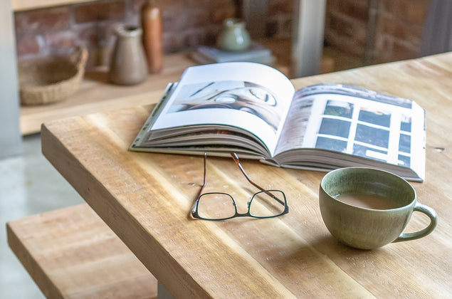 Wooden dining table with book, cup and glasses on top